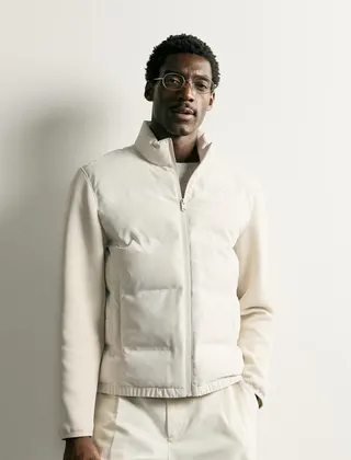 A man in a cream puffer jacket and cream trousers